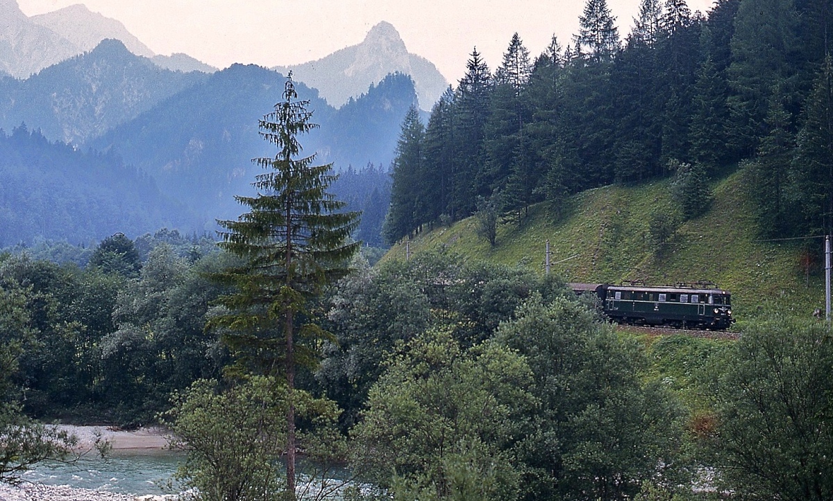 Landschaftlich äußerst reizvoll, aber wegen des Bewuchses nicht ganz so einfach mit Enns und Gebirge zu fotografieren ist die Gesäusebahn. Im August 1980 passte eine 1046 zwischen Johnsbach und Gestatterboden gerade so in eine Grünlücke (Neubearbeitung eines bereits veröffentlichten Bildes).