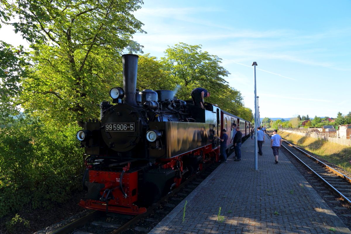 Langsam nähert sich am Abend des 07.07.2018 die Jubiläumssonderfahrt von 99 5906 mit ihrem IG HSB-Zug nun ihrem Ende. Gerade ist sie im Haltepunkt Nordhausen-Krimderode eingefahren und muß eine letzte Kreuzung, diesmal mit einer Nordhäuser Hybrid-Straßenbahn, abwarten. Gelegenheit für den Lokheizer zum  Endspurt  nochmals den Kohlevorrat umzuschichten.