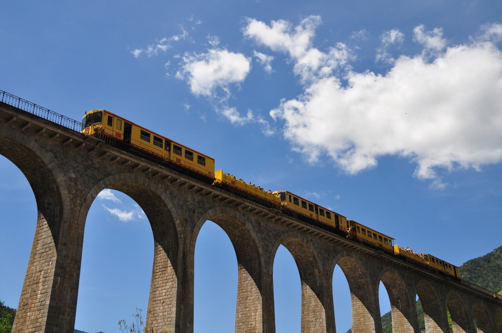 Le Petit Train Jaune am 14.08.2013 in der Mittagssonne auf dem Sjourn-Viadukt in der Nhe von Thus-entre-Valls in Sdfrankreich (Nhe Perpignan) Diese Touristenzge sind sehr beliebt und fahren mittels seitlich angebrachter dritter Strom-Schiene. Voran der Triebwagen mit der Nr.105. Ausgestattet ist ein gut besetzter Ganzzug zu touristischen Hochzeiten mit 2 Triebwagen und dazu mit mehreren zum Teil offenen  Cabriowagen .