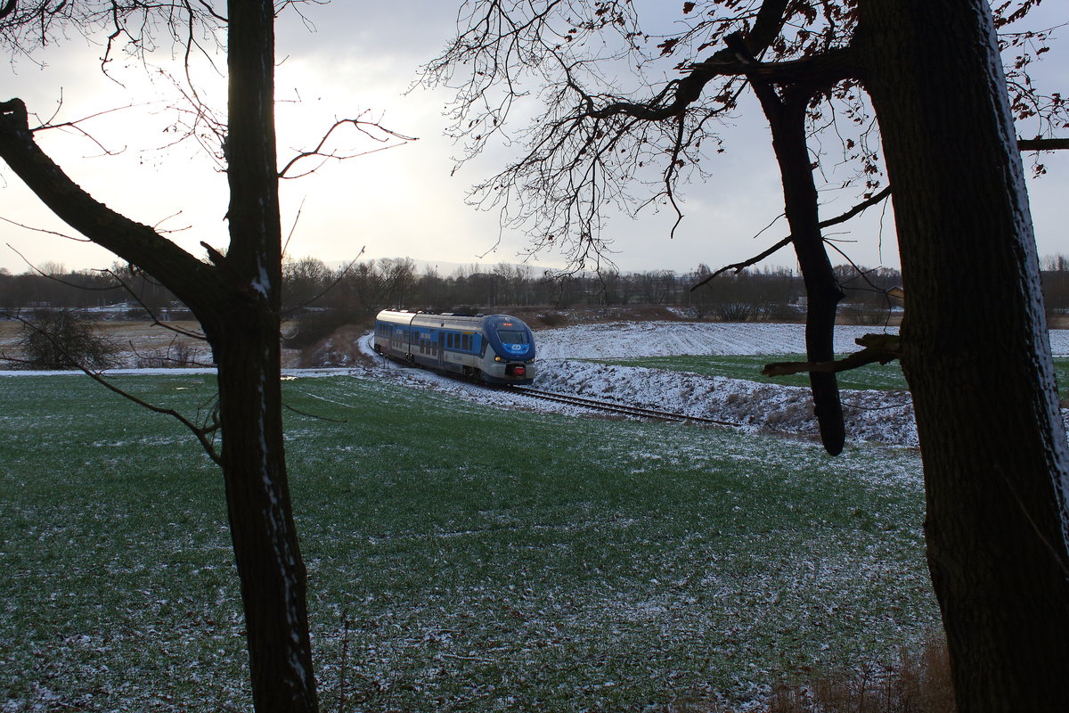 Leicht gepudert die Landschaft bei Tršnice mit dem OS nach Luby, die sonne kam bei der Durchfahrt des Regiosharks 844 004 fast noch durch die Wolken hindurch. Aufgenommen am 2.1.2019 