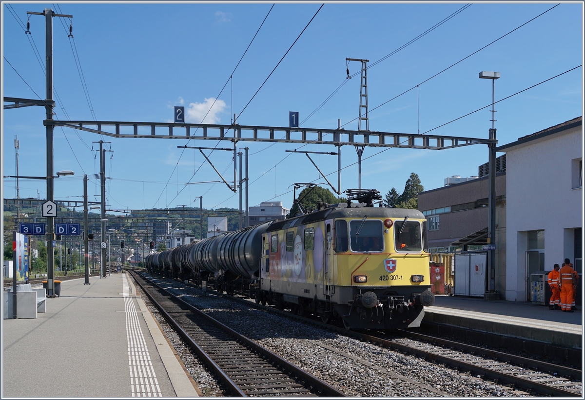 Leider mehr ein  Sichtungsbild  als ein sorgfältig gestaltetes Foto, denn als ich sah was da kommt war es zu spät, den Bahnsteig zu wechseln, wo ich dann ohnehin auf der  falschen  Seite gestanden hätte.
Ich habe aber trotzdem abgedrückt und zeige hier die Werbe Re 4/4 II 11307 (Re 420 307-1) mit einem Kesselwagenzug bei der Durchfahrt in Yverdon. 

3. Sept. 2020