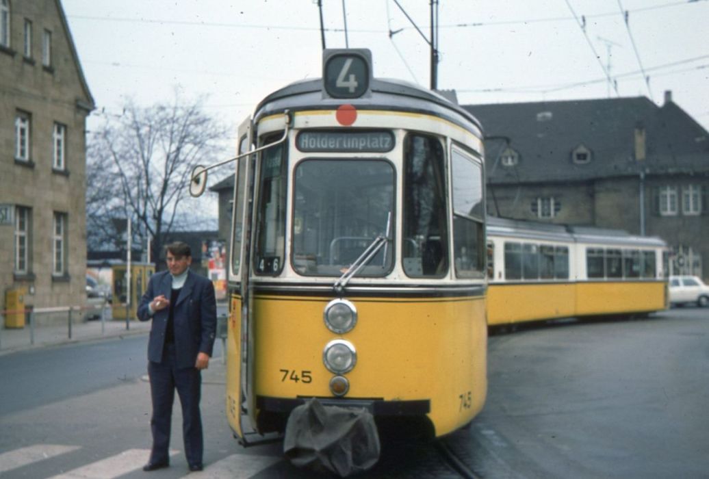 Linie 4, GT4 745 Kurs 4.6 vom Betriebshof Ostheim an der Endstation Obertürkheim, der Fahrer Hermann Joas macht Pause: Man beachte: roter Punkt (Fahrzeug hat Funk), Fenster links neben dem Fahrer noch in ursprünglicher Ausführung, weil damals noch keine Fahrerkabinen in die GT4 eingebaut waren.
Einzige Abtrennung zum Fahrgastraum war die gebogene Metallstange hinter dem Fahrersitz und abends konnte noch ein brauner Vorhang um den Fahrersitz herum zugezogen werden, als Schutz gegen Blendung aus dem Fahrgastraum. Außerdem Lackierung mit schwarz-gelbem Streifen am Dachrand, zweiteiliger schwarzer Zierstreifen mit Aluminiumzierleiste unterhalb der Fenster, sowie die Wagennummer in den großen eckigen Ziffern, wie im Auslieferungszustand. Schwach sichtbar auch die zweiteiligen Blinker am vorderen GT4 und die bereits einteiligen Blinker am geführten GT4. Das war 1977 das Unterscheidungskriterium zwischen diesen beiden GT4-Varianten.
Was man leider nicht sieht sind die schönen blauen Sitze im Fahrgastraum und der blaue Fahrersitz. Was man nur erleben konnte beim Mitfahren war, dass bei der 700er Serie der GT4 eine abweichende Fahrsteuerung zu einem wesentlich ruckfreieren Anfahren im Vergleich zu den älteren GT4 führte, was bei den Straßenbahnfahrern sehr beliebt war. 