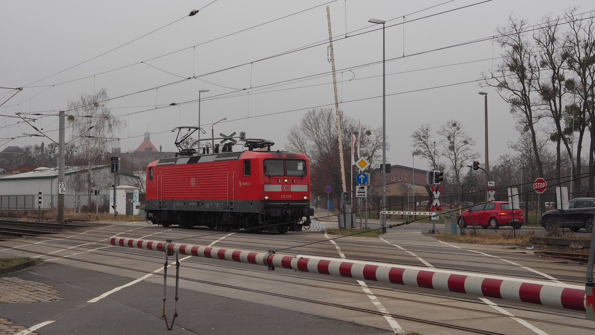 Lok 112 179 der DB Regio Nordost weilt derzeit im Ausbesserungswerk Dessau (LDX) und ist hier auf einer Probefahrt auf dem  AW-Anschlussgleis  am BÜ Elisabethstraße.

Der BÜ selbst hatte beim schlüsseln eine Fehlfunktion: Die Schranke der jew. Fahrtrichtung schloss sich, hingegen die der Gegenspur auf eigener Seite nicht. Im Bild zu sehen rechts hinter der Lok, der stehende Schrankenbaum und links am Bildrand der fehlende Baum auf meiner Seite. Nach 4 min Wartezeit wurde der BÜ vorsichtg von der Lok überquert und die Straße danach ohne Probleme wieder freigegeben.

Im Bildhintergrund verschindet an diesem diesigen Tag der Uhrenturm der ehemaligen Brauerei.

Dessau, der 05.02.2021