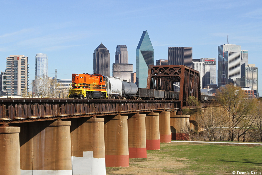 Lok 142, eine RP20PD, der „Dallas, Garland & Northeastern Railway“ rollt am 16.12.2014 mit einem Güterzug über die den Trinity River überspannende Brücke vor der Kulisse der Downtown Dallas.