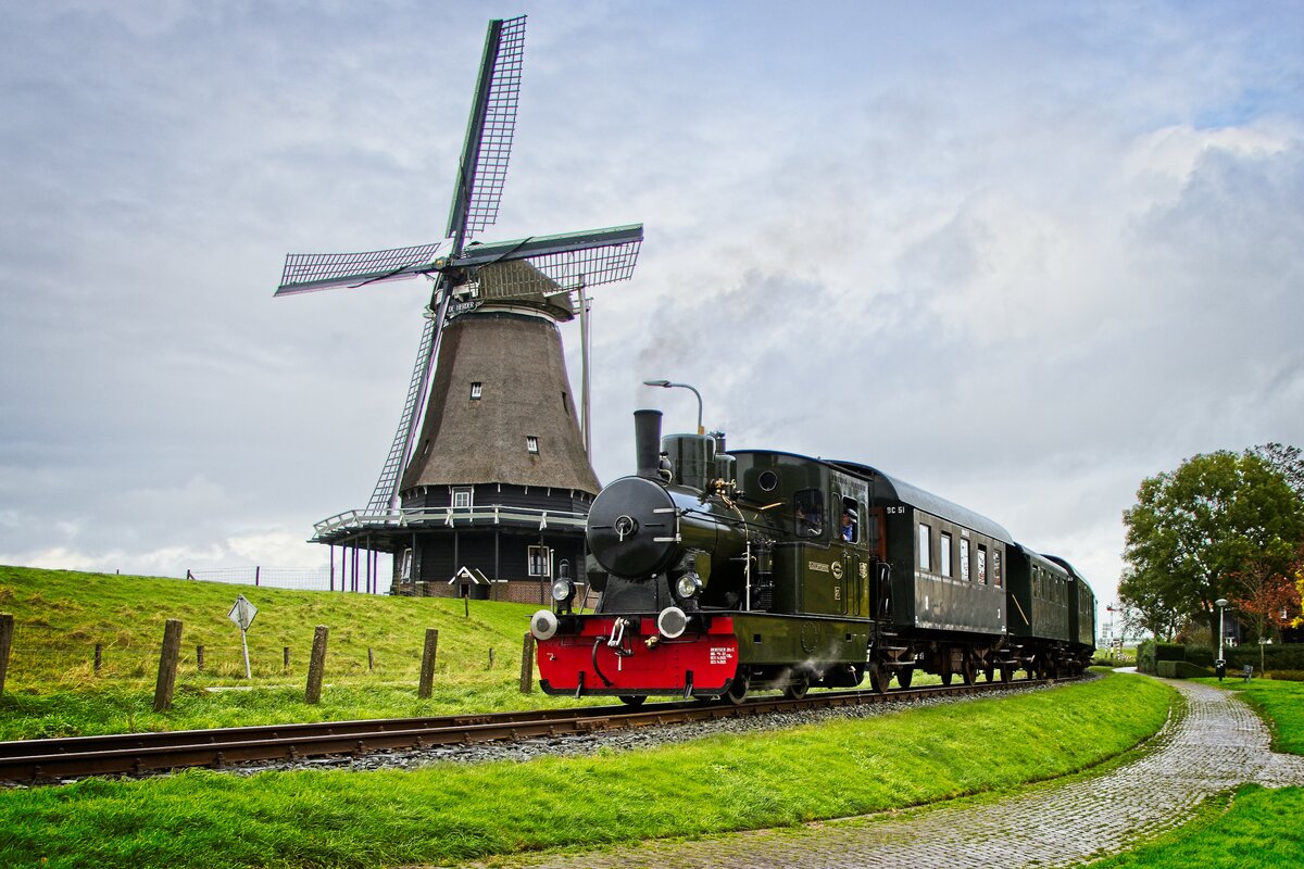 Lok 26 der ehemaligen Limburgsche Tramweg-Maatschappij passiert mit einem Lokalbahnzug die Mühle  De Herder  in Medemblik, Noord-Holland (22.10.2021)