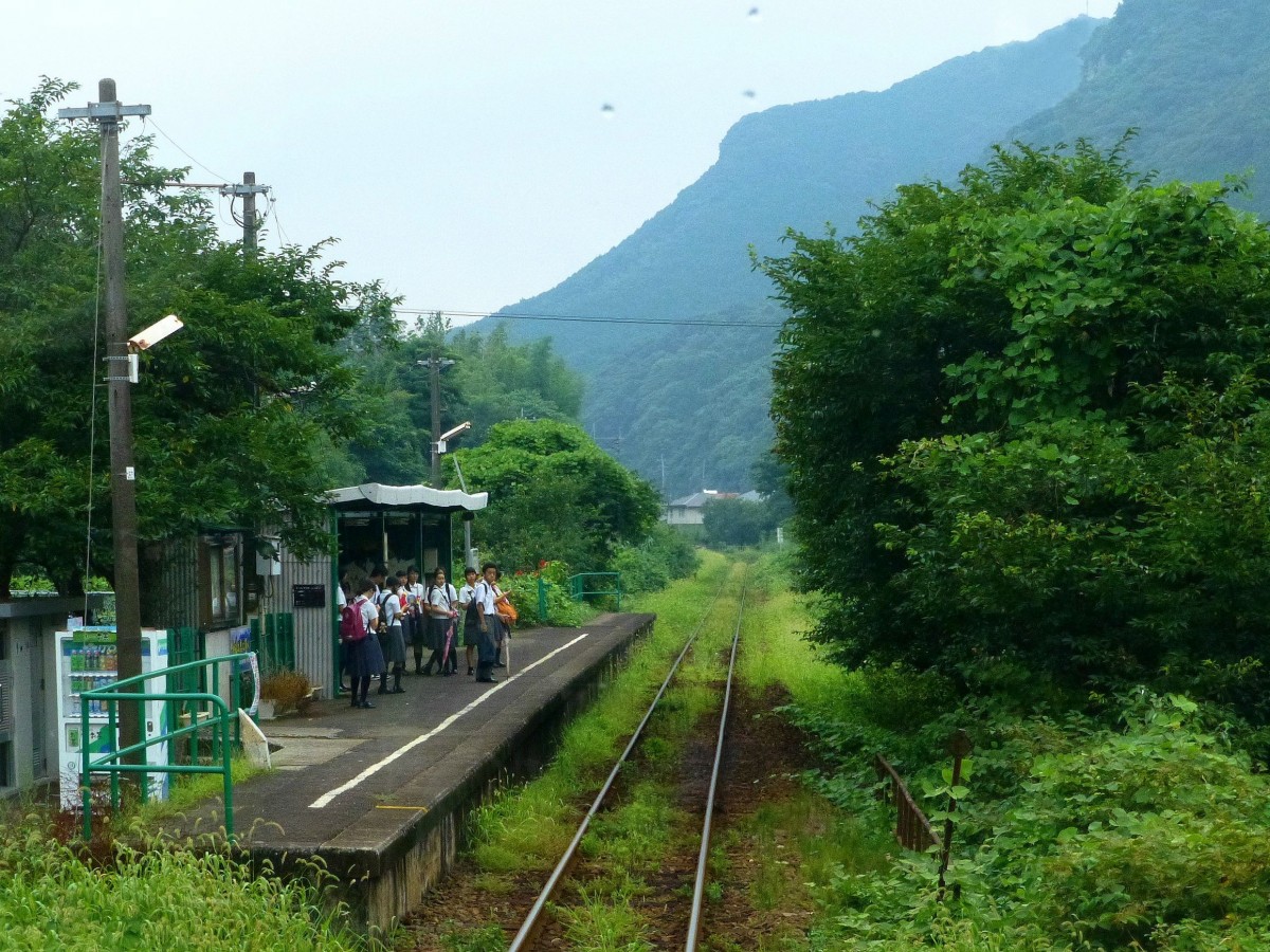 Matsuura-Bahn - Die Fahrgäste: Die wichtigste Aufgabe der Bahn ist die Beförderung von Schülern. Hier im dunstig-feuchten Tal neben der Seihô Kôkô-Oberschule. Bild aus Wagen 619, 26. Juli 2013. 