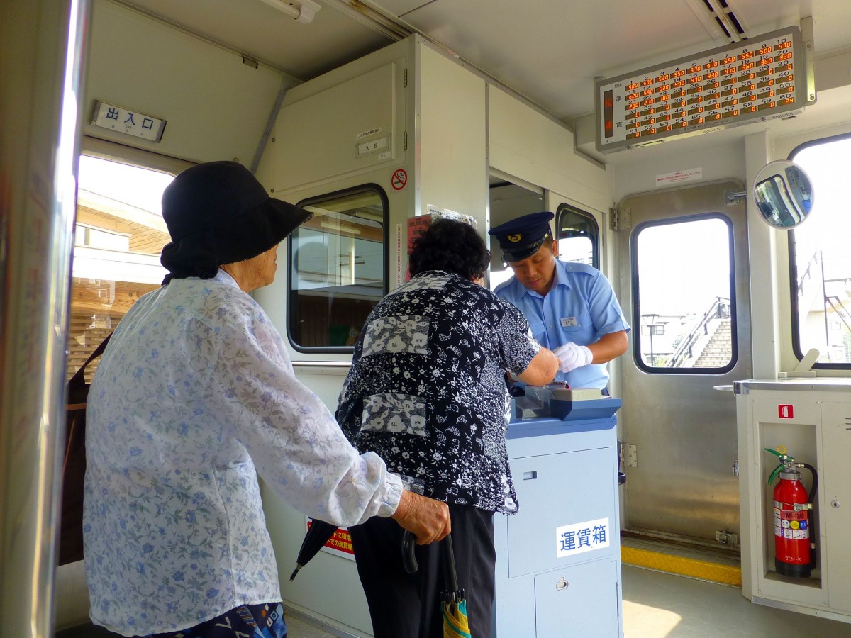 Matsuura-Bahn - Die Fahrgäste: Es sind praktisch nur alte Leute oder Schüler, welche die Bahn benutzen. Die alten Menschen sind stark auf die Hilfe der Wagenführer angewiesen. Er hilft ihnen auch, den jeweils korrekten Fahrpreis richtig in den Kasten zu werfen bzw. dafür Geld zu wechseln. Der Fahrpreis erscheint auf der Tafel rechts oben, wobei jede Station einer Nummer entspricht, die auf einem kleinen Zettel beim Einsteigen automatisch ausgegeben wird. Für die Fahrgäste wichtig ist auch die Erkennung des Namens des Wagenführers, der über dem Nichtraucherzeichen (in Bildmitte) vom jeweiligen Fahrer eingesetzt wird. Bild im Wagen 619, 26.Juli 2013. 