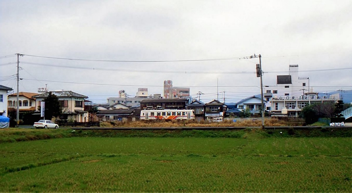 Matsuura-Bahn: Ein Wagen der Originalserie 101-111 (1988) huscht in Imari an einem kleinen Spital vorbei Richtung Arita. 25.März 1999. 