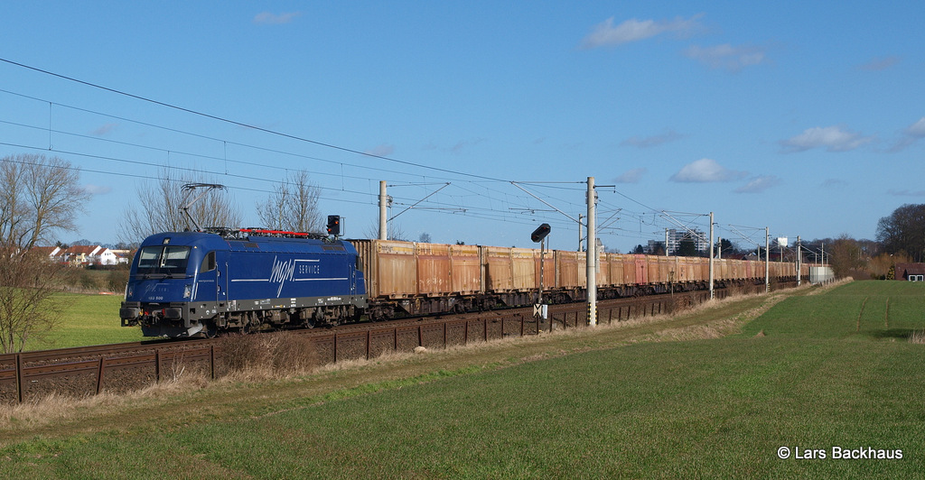 MGW 183 500 hat am 11.03.15 einen langen Hackschnitzelzug vom Lübecker Konstinkai am Haken und rollt nun durch Reinfeld Richtung Süden.