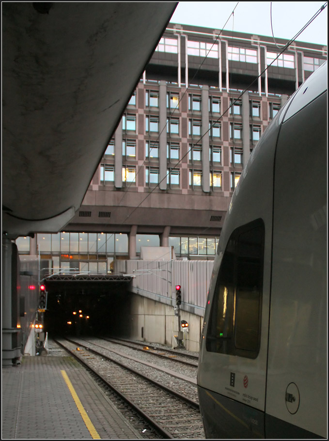 Mit der Bahn unter der Stadt hindurch -

Der 3,6 km lange Oslo Tunnel wurde 1980 eröffnet. Er verbindet die vorher von unterschiedlichen Bahnhöfen ausgehenden Bahnstrecken. Von Westen her endeten die Bahnstrecken im Kopfbahnhof Oslo Vestbanestasjon (Oslo V) und von Osten her in Oslo Østbanestasjon (Oslo Ø). Der Ostbahnhof wurde zum Hauptbahnhof ausgebaut und heißt heute Oslo Sentralstasjon (Oslo S). Im Empfangsgebäude des ehemaligen Westbahnhofes befindet sich heute das Nobel-Friedenszentrum, während die Züge nicht weit entfernt davon in der unterirdischen Station Nationaltheatret einen Zwischenhalt machen.

Der Oslo Tunnel ist nur einer von vielen Tunnels wenn man beispielsweise mit der Flughafenbahn vom Flughafen Gardermoen über Oslo nach Drammen fährt. Von etwa 97 km Streckenlänge liegen fast 42 km im Tunnel, der längste davon ist der 1999 eröffnete Romerika Tunnel östlich von Oslo an der Gardermoen-Bahn mit einer Länge von 14,580 km. 

Das Bild zweigt die Tunnel-Ausfahrt des Oslo Tunnels am Bahnhof Oslo S mit der Kopf eines neuen Stadler-Flirt-Triebwagenzuges, der hier im Regionalverkehr eingesetzt wird.

31.12.2013 (Matthias)
