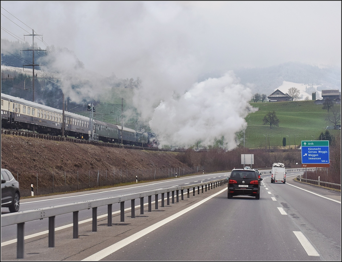 Mit Dampf zum Gotthard. Die etwas andere Stimmung wenn entlang der Autobahn 01 202 ihren Sonderzug Richtung Bergstrecke bringt und gut, dass sich die Dampfwolke nicht ganz auf die Fahrbahn senkt. Direkt an den Kantonsgrenzen Luzern, Schwyz und Zug, März 2018.
