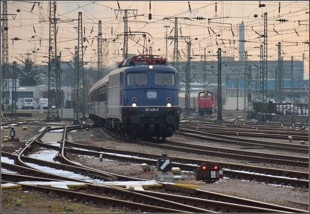 Mit Dampf zum Gotthard. Nach der Übernachtung werden die Fahrgäste in Konstanz und Singen eingesammelt. 110 428-0 fährt mit ihrem langen Zug nach Singen ein. Es sieht fast ein bisschen aus wie zu Bundesbahnzeiten, die rangierende V 60 im Hintergrund rundet trotz verkehrsrotem Outfit die Szene ab. März 2018.