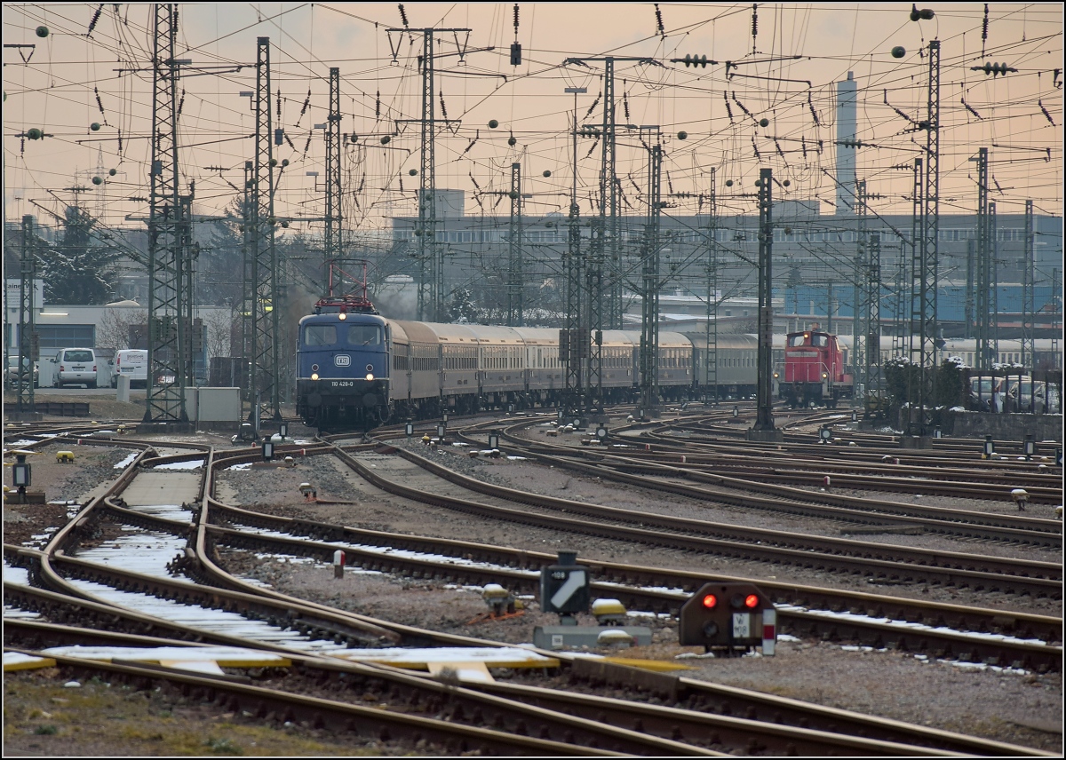 Mit Dampf zum Gotthard. Nach der Übernachtung werden die Fahrgäste in Konstanz und Singen eingesammelt. 110 428-0 fährt mit ihrem langen Zug nach Singen ein. Es sieht fast ein bisschen aus wie zu Bundesbahnzeiten, die rangierende V 60 im Hintergrund rundet trotz verkehrsrotem Outfit die Szene ab. März 2018.
