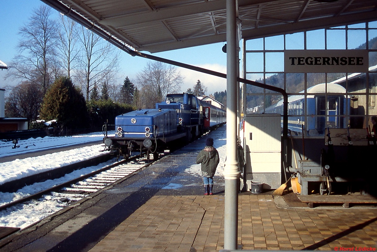 Mit dem Generatorwagen voraus fährt Lok 14 der Tegernsee-Bahn im Januar 1991 im Bahnhof Tegernsee ein. Bei der Lok handelte es sich um eine 1982 von MaK gebaute B'B'-dh des Typs G 1203 BB, die nach der Übernahme des Betriebs durch die BOB im Jahre 1999 an Stern & Hafferl in Österreich verkauft wurde. Da die Lok über keine Einrichtung für elektrische Zugheizung verfügte, beschaffte die TAG den Generatorwagen. Rechts im Bild ein ex-DB-Wagen der TAG.