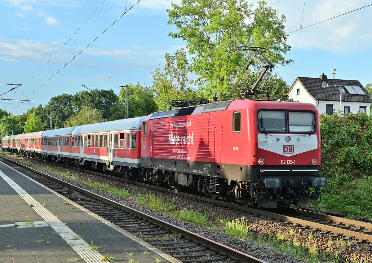 Mit dem RE 12a vorm Latz kommt am Montagabend die 112 139-1 in Offenau eingefahren. Da der N-Wagenzug länger ist als der Dostockwagenzug, stellt die Lok dann den Bü an der Bahnhofstraße für die Dauer des Haltes zu. 15.8.2022