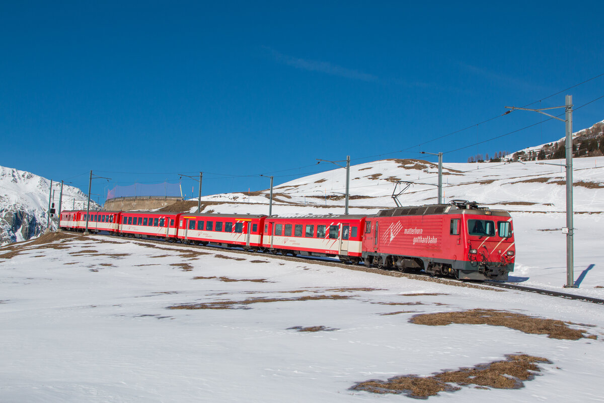 Mit dem Regionalzug von Disentis nach Andermatt hat die HGe 4/4 II mit der Nummer 2 soeben den Bahnhof Nätschen verlassen und rollt den Berg nach Andermatt hinunter. Fotografiert am 10.02.2023.  
