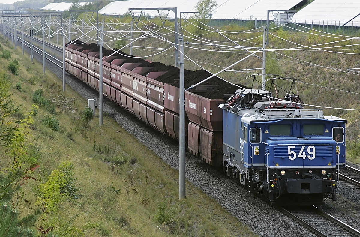 Mit einem beladenen Braunkohlezug ist die Lok 549 von RWE Power (Typ EL 1, Krauss-Maffei 18209/1956) am 02.09.2020 bei Kerpen-Buir auf der Hambachbahn unterwegs (Bildausschnitt). Außer der Spurweite haben die Züge auf dem rund 230 km langen Netz, das die Tagebaue mit den Kraftwerken verbindet, mit dem DB-Netz nicht viel gemeinsam: Die elektrischen Strecken werden mit Einphasenwechselstrom von 6,6 V und 50 Hz betrieben, die Lokomotiven haben eine Achslast von 35 t und die Braunkohlewagen ein Lichtraumprofil von 4 m.