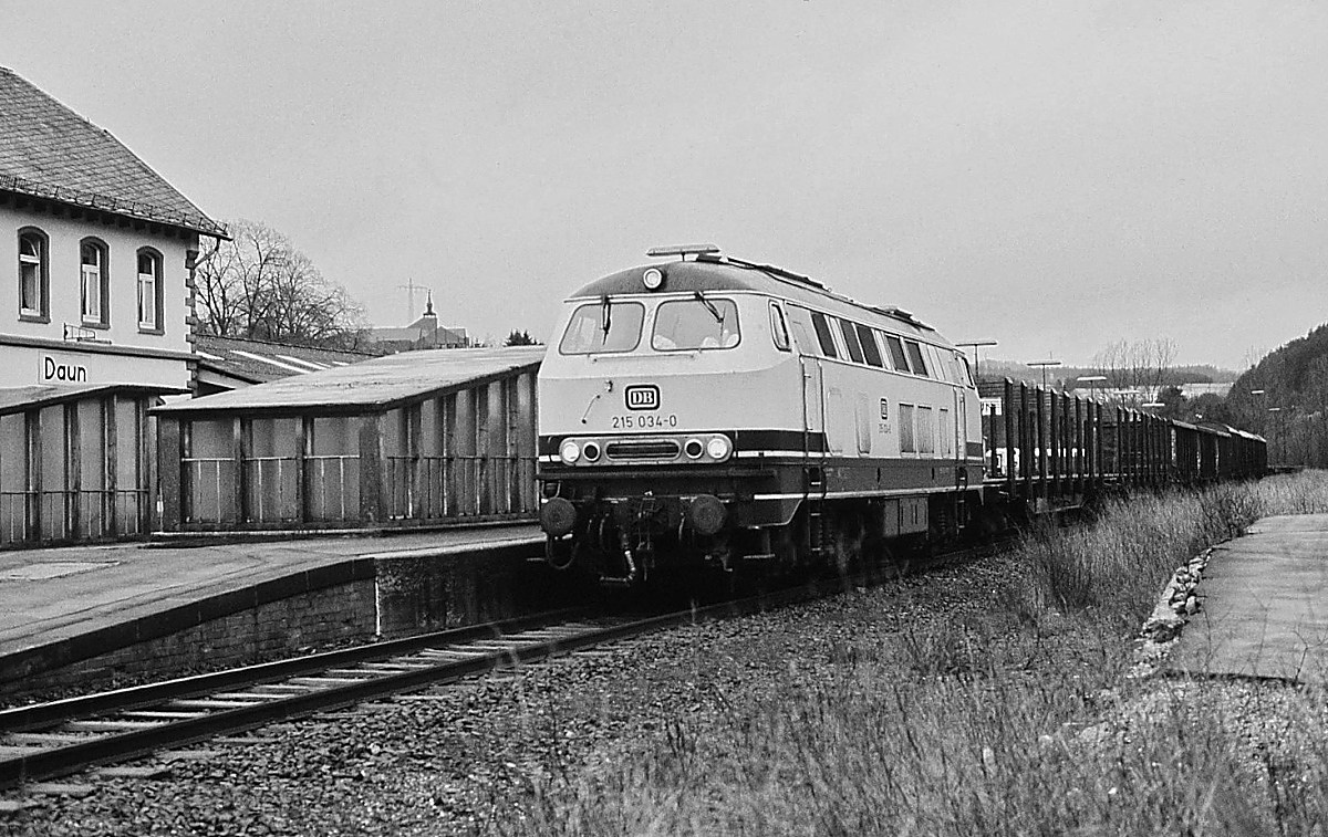 Mit einem Güterzug wartet 215 034-0 im Bahnhof Daun auf die Weiterfahrt (Frühjahr 1989)