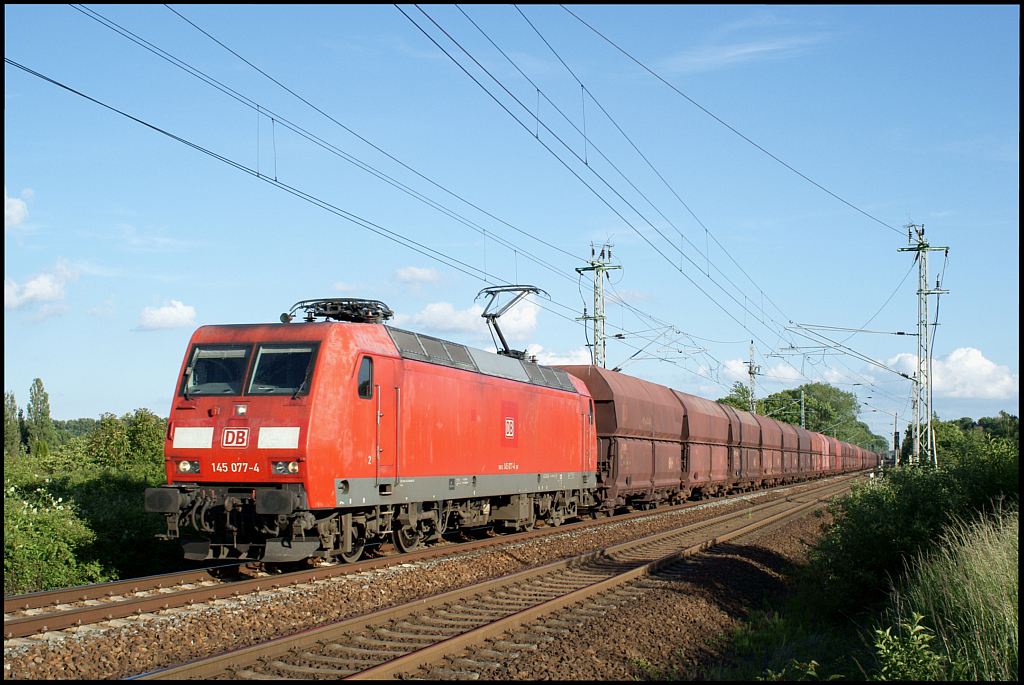 Mit einem hochwasserbedingt umgeleiteten Bunkerzug ist 145 077-4 am 10.06.2013 in der Nähe des Abzweigs Srg in Richtung Rostock unterwegs.