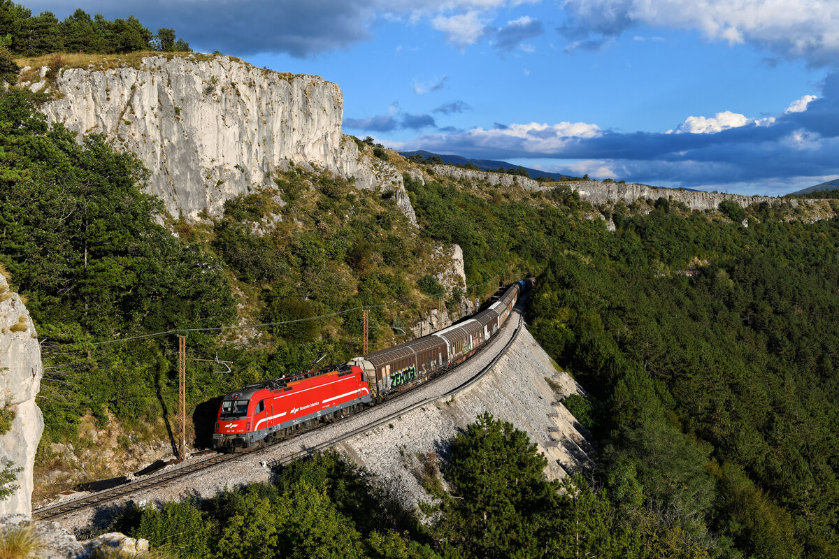 Mit einem langen Ganzzug, bestehend aus vierachsigen Schiebewandwagen, kam am Abend des 18. September 2021 die 541 105 die Koper-Rampe heraufgefahren. Bei Črni Kal konnte ich den Zug mit dem Karstgebirge im Hintergrund aufnehmen. Die Tauri der Slowenischen Staatsbahn wickeln den Großteil des Güterverkehrs auf der anspruchsvollen Gebirgsstrecke ab. 