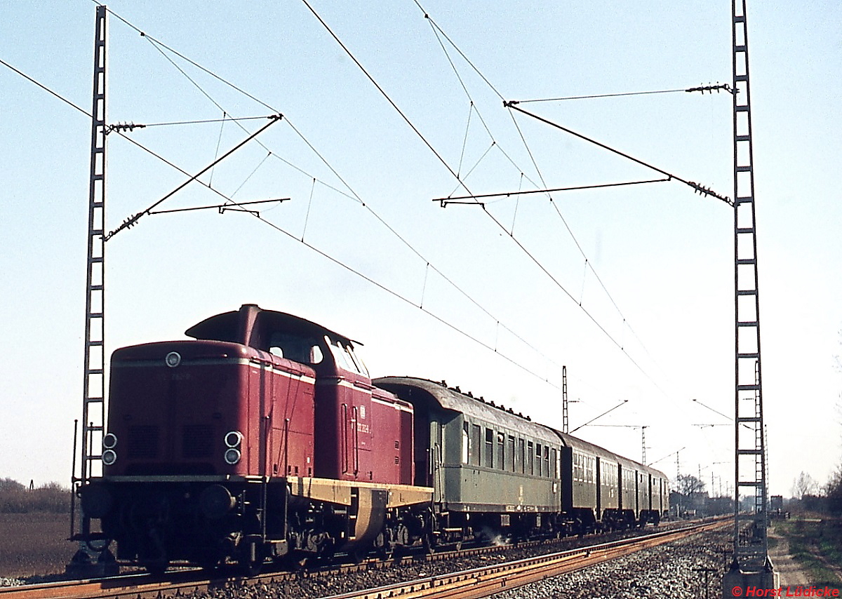 Mit einem Nahverkehrszug hat sich eine 212 im Februar 1975 auf den Weg von Rheine in Richtung Emden gemacht. Neben Umbau-Vierachsern kamen in diesen Zügen damals auch noch Vorkriegs-Eilzugwagen zum Einsatz. Zu diesem Zeitpunkt standen bereits die Masten für die elektrische Strecke nach Bad Bentheim, die in Salzbergen von der Emslandstrecke abzweigt und auf der am 01.06.1975 der elektrische Betrieb aufgenommen wurde. 