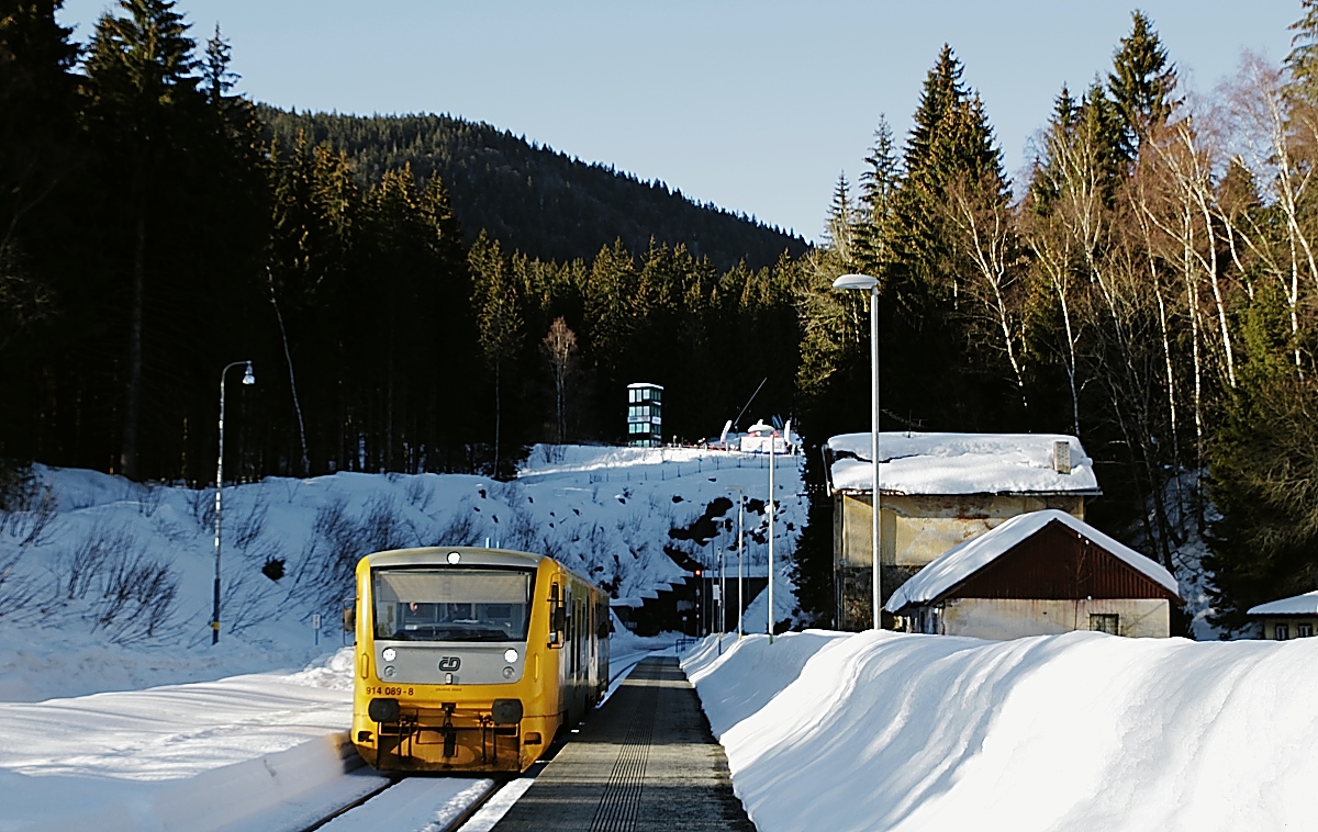 Mit einem Os kommt 814/914 089 am 16.02.2019 im 840 m hoch gelegenen Bahnhof Spicak an, im Hintergrund der 1.747 m lange Spicacky/Spitzbergtunnel, Scheitelpunkt der Strecke von Klatovy nach Zelesna Ruda-Alzbetin 