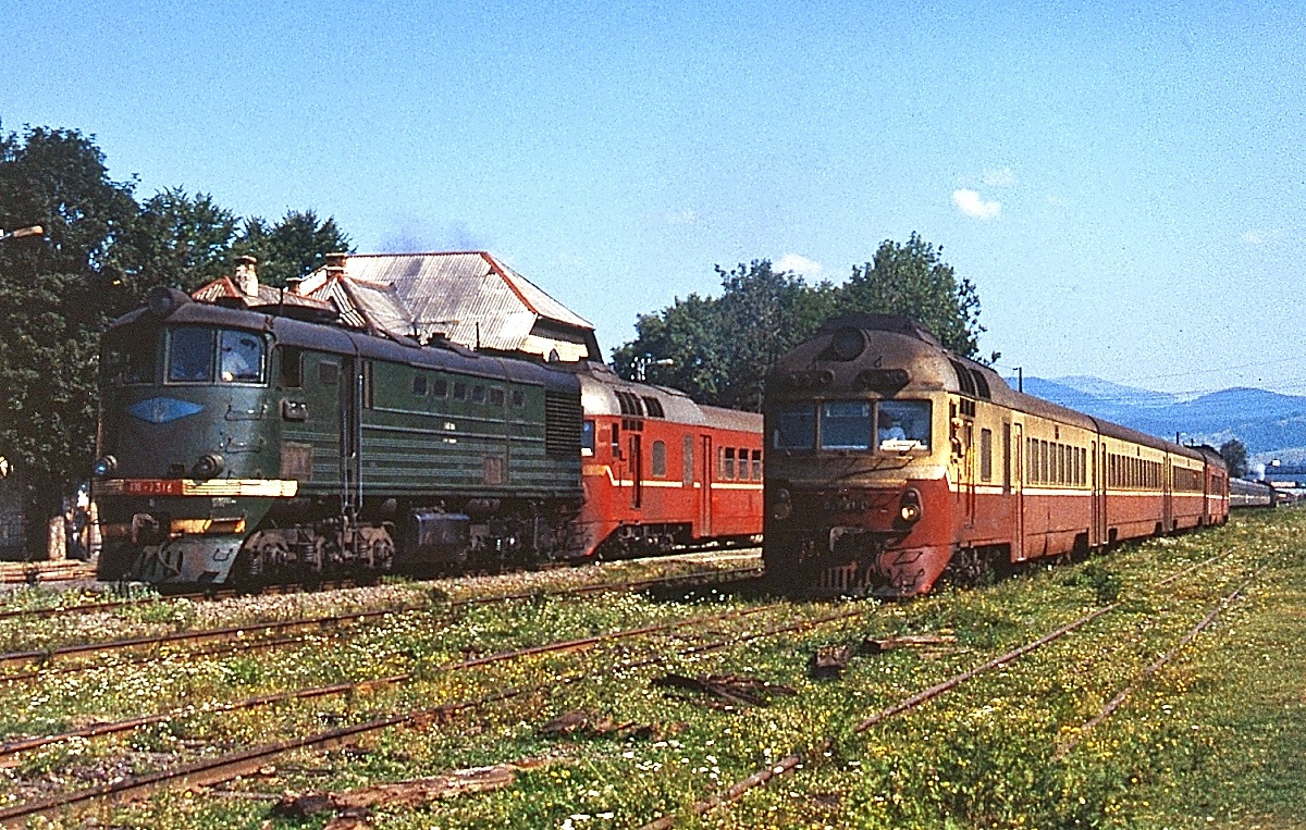 Mit einem Triebwagen der Reihe D1 im Schlepp fährt eine unbekannte TE3 aus dem Bahnhof Jassinja an der Karpatenstrecke von Rachiv nach Iwamo-Frankiwsk aus, daneben ein weiterer D1
