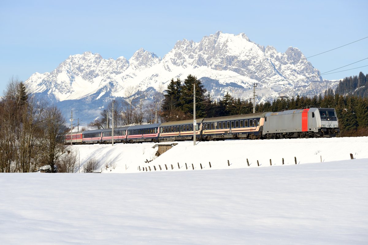 Mit einer Verspätung von etwas über einer Stunde kam am 06. Februar 2016 der zweite Turnuszug des Tages in Fieberbrunn durch. D 13897  Treski  von Brüssel Midi nach Bischofshofen wurde an diesem Tag von der Railpool 185 679 befördert. Die Lok fährt seit kurzem für Lokomotion und hebt sich durch den roten Streifen von den anderen Loks des Vermieters ab. Vorher wurde sie einige Jahre in Norwegen und Schweden eingesetzt. Die belgischen Liegewagen heben sich gut von von der verschneiten Landschaft ab. Über allem thront das Wilde Kaiser Gebirge.