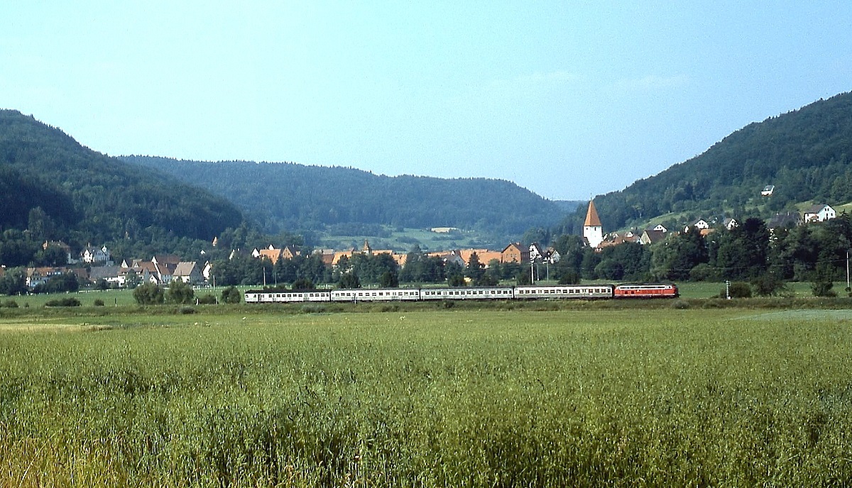 Mit vier Silberlingen im Schlepp ist eine unbekannte 218 im Juli 1985 vor der Kulisse von Eschenbach in Richtung Nürnberg unterwegs