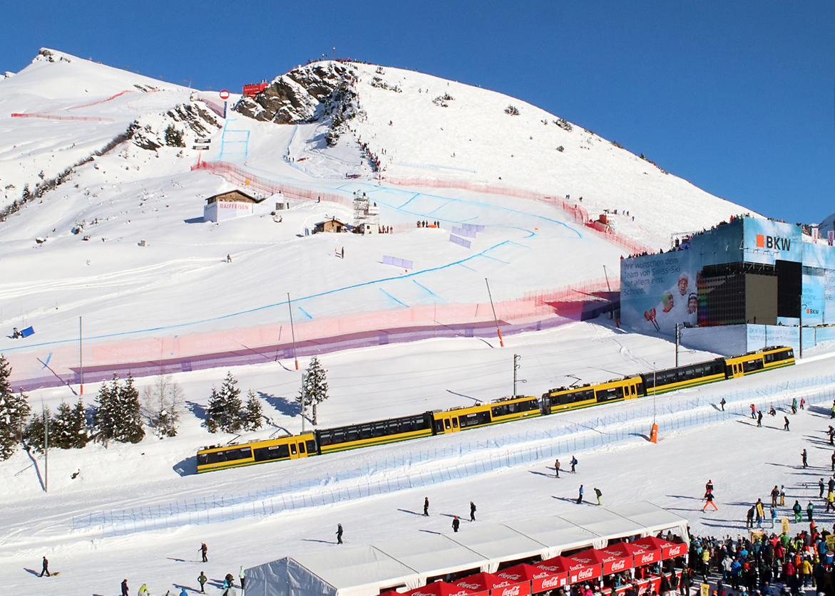 Mit der Wengernalpbahn kommt man problemlos an die interessanteste Stelle der Lauberhornabfahrt im Ski-Weltcup. Der Fotograf steht hier am Girmschbiel (nur wenige Minuten zu Fuss ab der Station Wengernalp erreichbar) mit Blick auf den so genannten Hundschopf (enge Passage oben), die Minschkante (Bildmitte) und den Canadian Corner (rechts). Hier ist für die Verpflegung reichlich gesorgt, die Zuschauer veranstalten jeweils ein richtiges Volksfest. Im Vordergrund fährt die WAB von Lauterbrunnen - Wengen nach Wengernalp - Kleine Scheidegg. Wengernalp, 11.1.2024