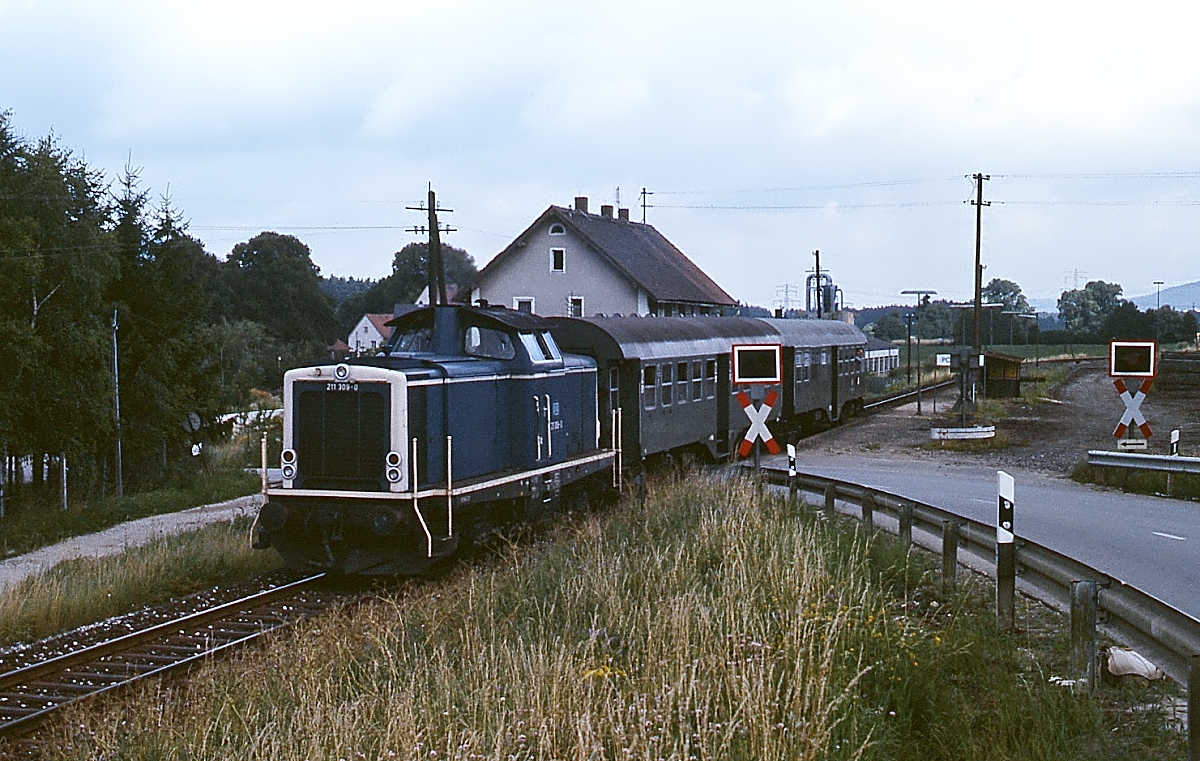 Mit zwei Umbau-Vierachsern verlässt 211 309-0 im Juli 1987 den Haltepunkt Pollanten an der Bahnstrecke von Neumarkt nach Beilngries. Seit dem 25.09.1987 verkehren hier keine Züge mehr.