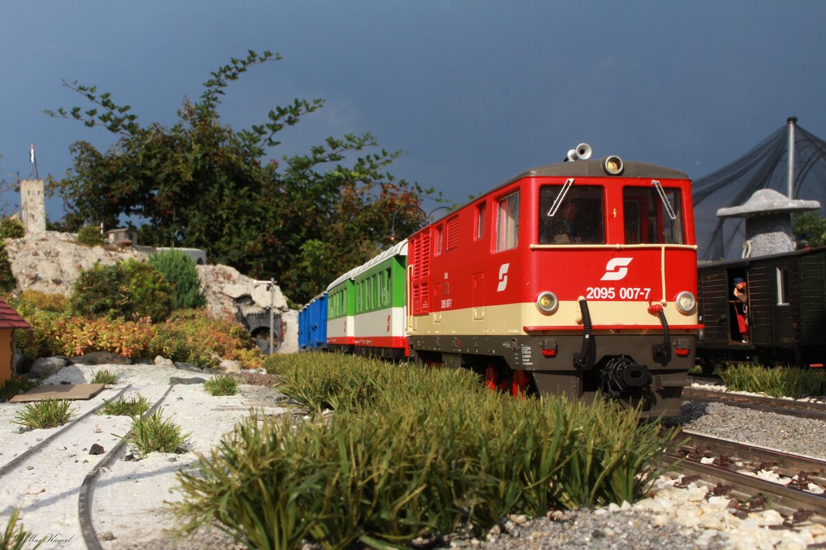 *Modell*
Mit gut 25 Minuten Verspätung fährt die 2095 007 im August 1996 mit einem Personenzug von Garting nach Brunn am Berg hier im Bahnhof Wisach.
Wegen dem aufziehenden Gewitter sind die beiden Radwagen voll beladen und die Personenwagen voll besetzt mitn Radausflüglern die ins trockene geflüchtet sind.