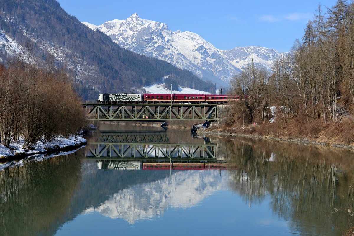 Nach Ankunft in Schladming fährt der Alpen Express als Lp 85104 zurück nach Bischofshofen. Dort wird der Wagenpark hinterstellt, behandelt und gesäubert. Am 11. Februar 2017 erwartete ich diese Leistung am Ufer der Salzach bei Bischofshofen. In langsamer Fahrt überquerte 151 074 mit ihrem Zug die Brücke und glücklicherweise erlaubte der ruhig dahin fließende Fluss erneut eine Spiegelung des Sechsachsers mit dem Turnuszug und der eindrucksvollen Bergkette des Hagengebirges im Hintergrund.