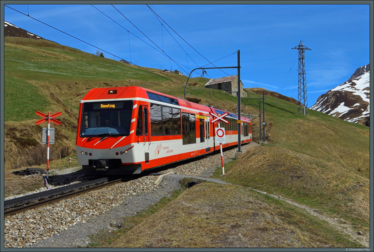 Nach einem Einsatz am Oberalppass rollt ABDeh 4/8 2023 wieder hinab ins Tal nach Andermatt. Gerade hat der Triebwagen einen der Kehrtunnel verlassen und quert einen kleinen Bahnübergang am Hang des Nätschen. (19.04.2022)