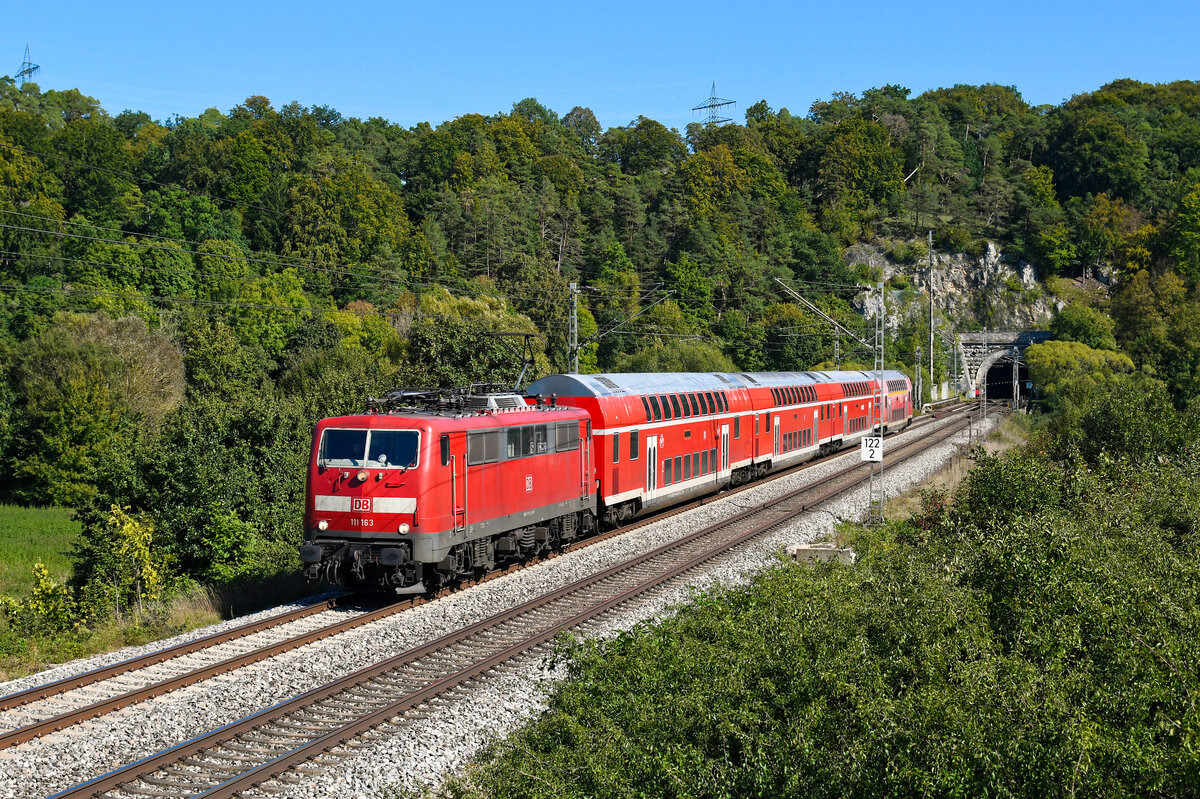 Nach wie vor unverzichtbar sind die Loks der Baureihe 111 bei DB Regio in Bayern. Allerdings ist der Bestand in München und Nürnberg auf inzwischen nur noch knapp über 20 Loks zusammengeschrumpft. Eine davon ist die optisch recht gepflegt wirkende 111 163. Sie war zuletzt lange Zeit in Stuttgart beheimatet und verstärkt seit Ende 2019 den Münchner Bestand. Am 25. September 2023 bespannte 111 163 die RB 59154 nach Nürnberg HBF. Der Zug verkehrte anstelle des planmäßigen Triebzug der Baureihe 445. Entstanden ist die Aufnahme bei Esslingen im Altmühltal, kurz nach Verlassen des gleichnamigen Tunnels.