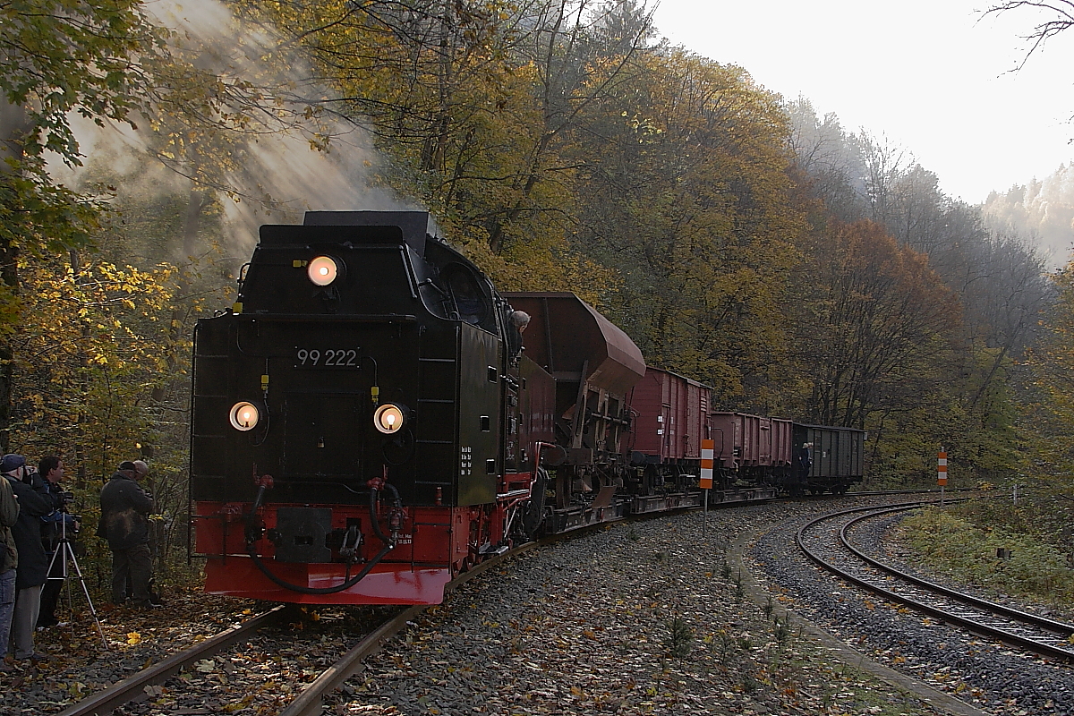 Nachdem 99 222 mit dem Fotgütezug der HSB am 19.10.2013 eine Doppelausfahrt mit Planzug P8904 aus dem Bahnhof  Eisfelder Talmühle  absolviert hat, drückt sie ihren Zug jetzt zurück in den Bahnhof. Besonders gefielen mir hier die schräg durch Rauchwolke und Laub einfallenden Sonnenstrahlen!

(Anmerkung zum Aufnahmestandort: Der Standort befindet sich an der Waldzunge genau zwischen der Gleisgabelung von Selketal- und Harzquerbahn, kurz hinter dem Bahnhof  Eisfelder Talmühle . Die Doppelausfahrt war speziell zu einem Fototermin für die Fahrgäste eines Sonderzuges der IG HSB organisiert (geplanter Bestandteil der Sonderfahrt), der Standort vorher genau festgelegt, von der Betriebsleitung der HSB genehmigt und durch Mitarbeiter der IG HSB überwacht und abgesichert worden, welche mit Argusaugen und Warnweste sowie  Meckertüte  (Megafon) bewaffnet, genauestens darauf achteten, dass keines ihrer  Schäfchen , und das waren immerhin 30-40, verlorenging oder sich gar in Gefahr brachte. Ich versichere, dass die Aufnahme somit absolut legal und keinesfalls eigenmächtig entstand!)