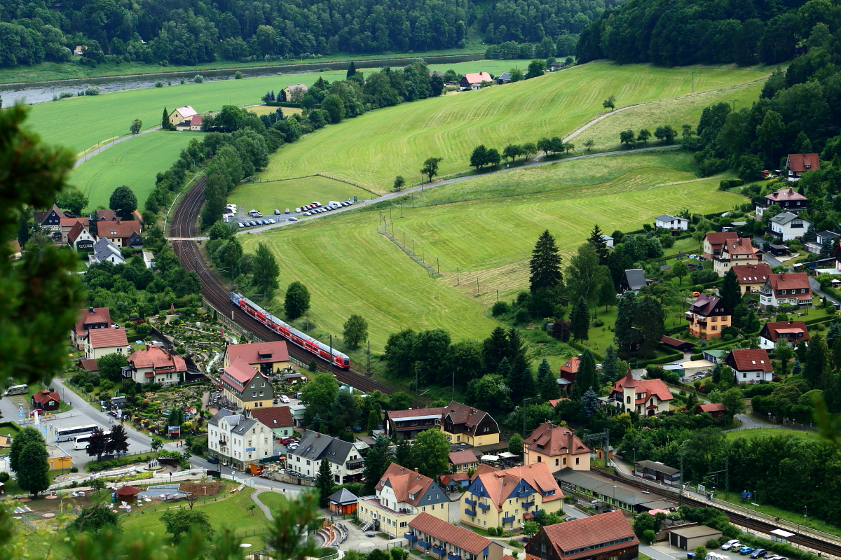 Nachdem am 16.06.2017 ein Dresdener S-Bahnzug den Haltepunkt Kurort Rathen verlassen hat, strebt er jetzt in Richtung Schöna. Nächster Halt ist Königstein. Direkt links neben dem Zug ist das Gelände der  Eisenbahnwelten Rathen , der, laut Betreiber, weltweit größten Gartenbahnanlage, zu erkennen.