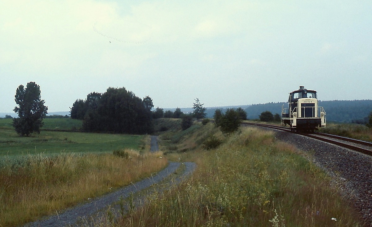 Nachdem sie vormittags die Nebenbahn nach Tirschenreuth bedient hatte, brachte 260 112-8 am Nachmittag dieses Julitages 1985 eine Übergabe nach Waldsassen, zurück ging es mangels Fracht als Lz, hier im dünn besiedelten Grenzland zwischen Waldsassen und Steinmühle. Die Bahn führte bis zum Ende des zweiten Weltkrieges weiter in das tschechische Eger/Cheb und war als Hauptbahn klassifiziert. Der Personenverkehr wurde 1986, der Güterverkehr zwischen Mitterteich und Waldsassen 1994 eingestellt.