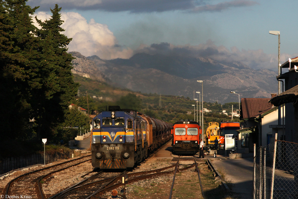 Nachdem wir den Nachtzug B 1205 bei Sadine erfolgreich fotografiert hatten, wollten wir fr den nachfolgenden 60340 nach Kastel Stari an das bekannte Motiv mit dem Kirchenblick. Doch leider kam der 60340 schneller als wir es erhofft hatten und so war bei unserer Ankunft in Kastel Stari der Bahnbergang am Bahnhof bereits geschlossen und es war nur noch schnell dieser Notschuss von der Laderampe auf den Bahnhof mglich. Whrend der 60340 angefhrt von 2062 119 den Bahnhof durchfhrt, wartet rechts 7122 023 auf die Fahrt nach Split. (28.08.2013).