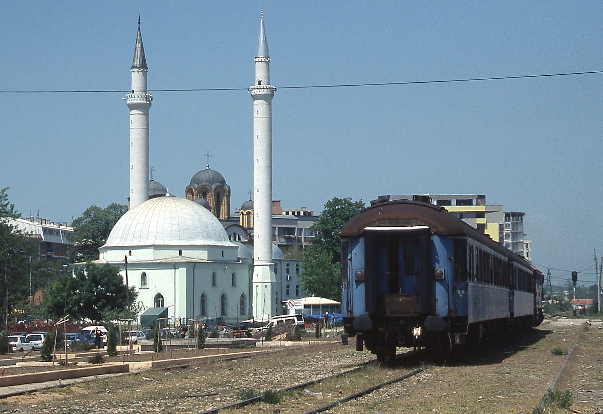 Nachschuß auf den Intercitiy von Skopje nach Fushe Kosove/Kosovo Polje, der mit Lok 008 am 14.05.2009 den Bahnhof Ferizaj/Urosevac verläßt. Hinter der neuen Moschee ist die Kuppel einer orthodoxen Kirche sichtbar.