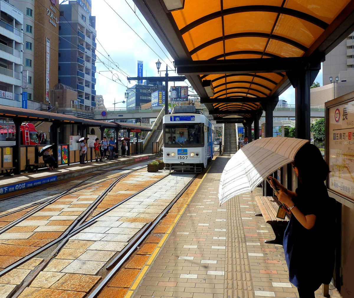 Nagasaki Strassenbahn – aus Gebrauchtmaterial zusammengebaute Wagen, Serie 1500. 1993-97 erstellte Wagenkasten (Nr. 1501-1507) unter Verwendung grösstenteils von Gebrauchtmaterial. Neuer einarmiger Pantograph. 2x45 kW Motoren. 1507 seit 2010 mit neuer Steuerung. Wagen 1507 fährt in die Haltestelle  Hauptbahnhof  ein. 8.August 2013 