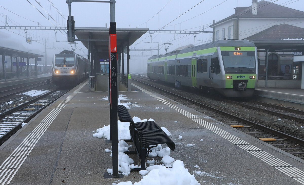 Nebliger Morgen am Bahnhof Murten: Gerade ist ein Güterzug eingefahren, geführt von der durch die BLS gemieteten Railpool Lokomotive 187 004. Rechts wartet die BLS NINA 525 003 auf Rückfahrt als S5 nach Bern. 14.Dezember 2021  