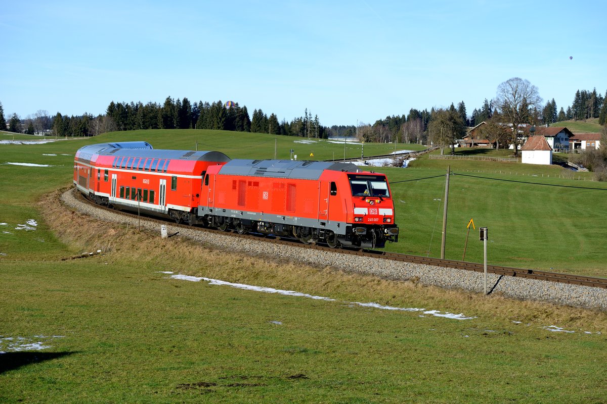 Noch etwas gewöhnungsbedürftig sind die Doppelstockwagen mit der Baureihe 245 auf der König-Ludwig-Bahn. RE 57506 nach Füssen konnte am 06. Januar 2015 kurz vor Erreichen des Bahnhofes Weizen-Hopferau aufgenommen werden. Es führt die 245 007. Bedauerlicherweise hatte der Zug  +2 , wäre er pünktlich gewesen, wäre der gerade noch hinter dem Waldstück verschwindende Heißluftballon schön im Bild gewesen...