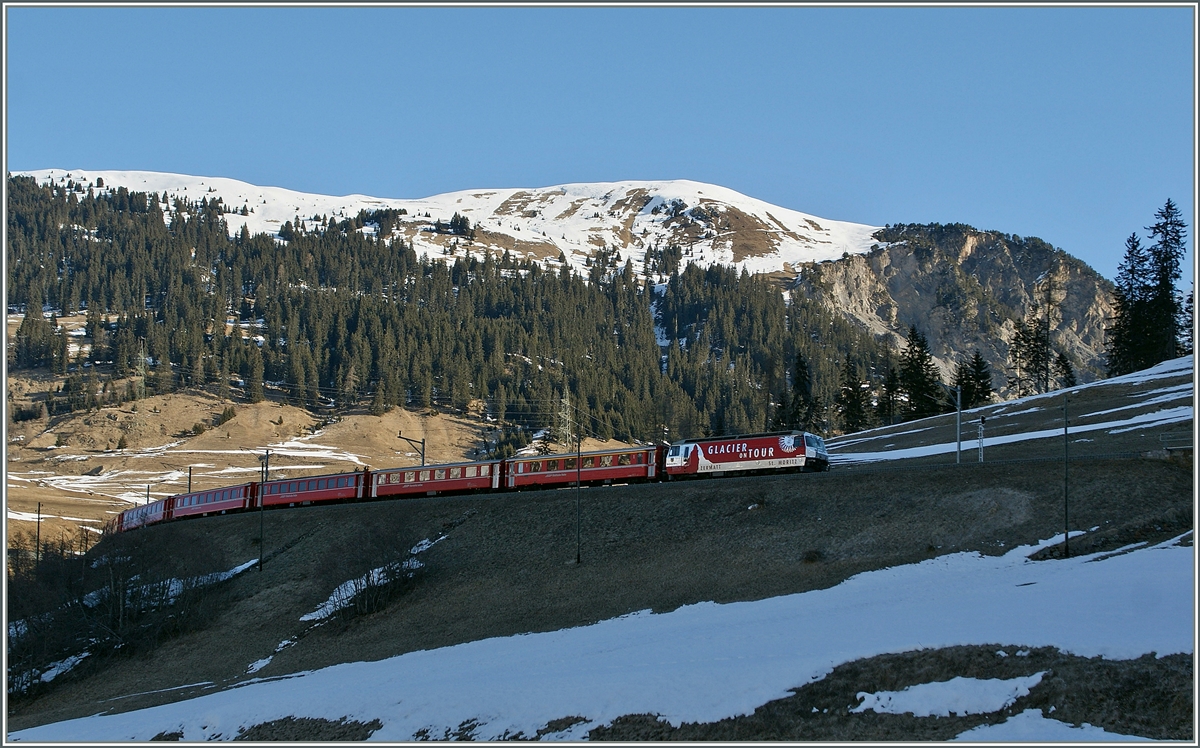 Noch liegt das Tal im Schatten doch die RhB  Glacier Express  Ge 4/4 III leuchtet schon in den kühlen März Morgen. 
Oberhalb von Bergün, den 16. März 2013