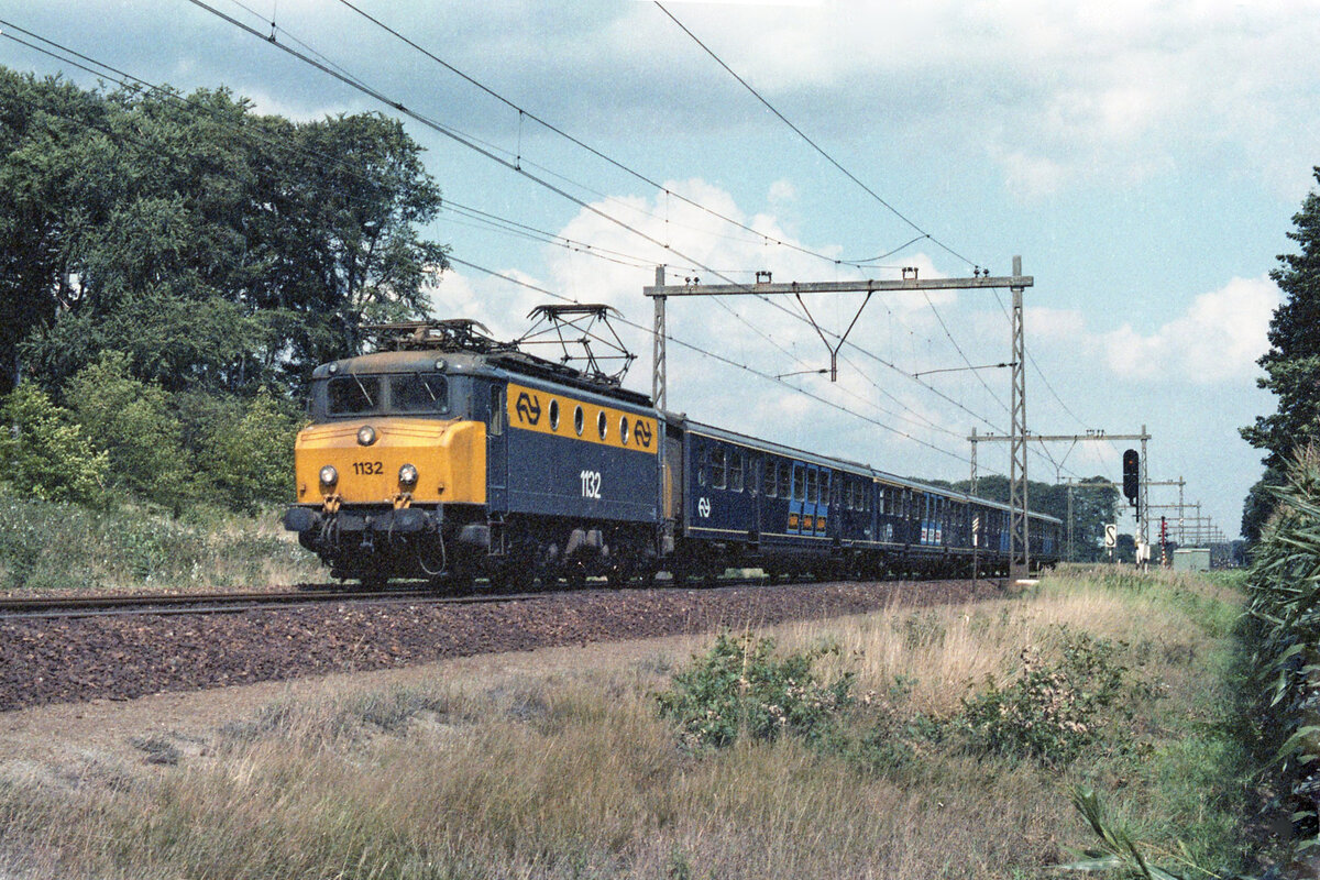 NS 1132 mit Zug 4353 (Zwolle - Roosendaal) südlich Dieren am 19.08.1982. Lok der Reihe 1100 mit Wagen vom Typ Plan E. Vom Rande eines Maisfeldes konnte ich den Zug fotograferen; heute hat sich das Ganze total verändert: eine Autobahn verläuft jetzt an dieser Stelle neben der Bahnstrecke. Scan (Bild 92856, Kodacolor 400).