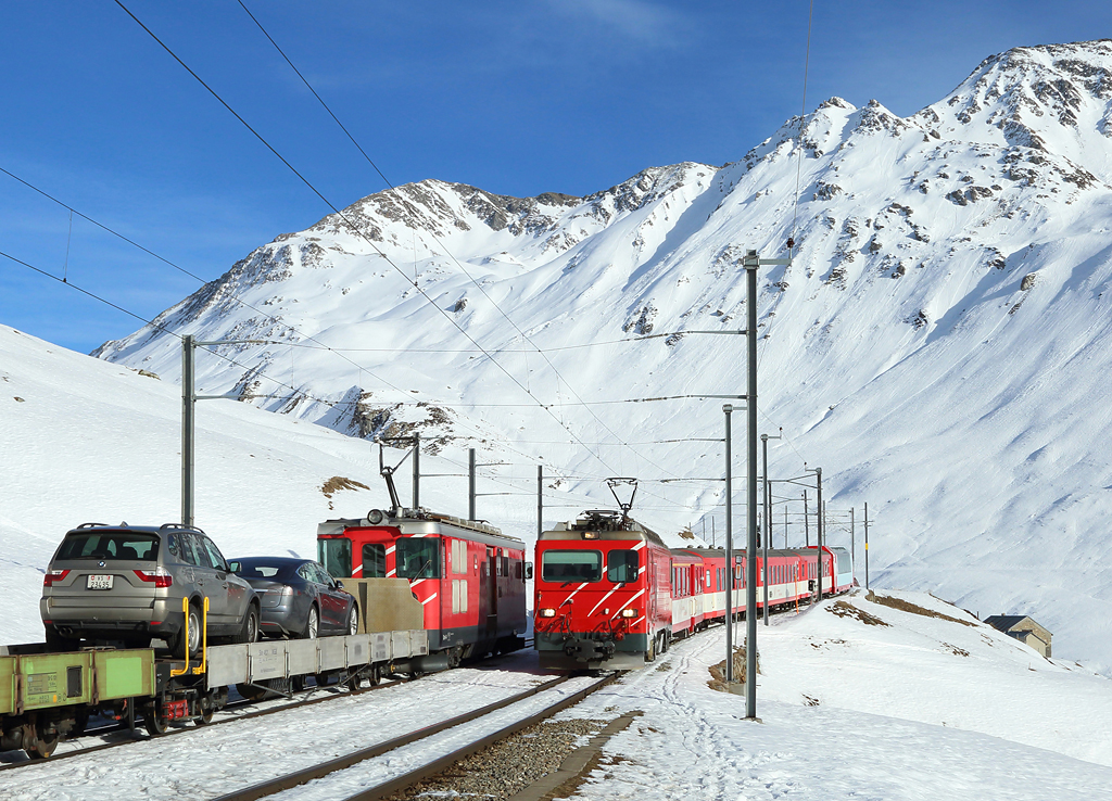 Number 2 approaches Nätschen whilst working train 843, 1414 Disentis-Andermatt. 

The Andermatt-Sedrun autozug waits to enter the single line, 2 Feb 2016