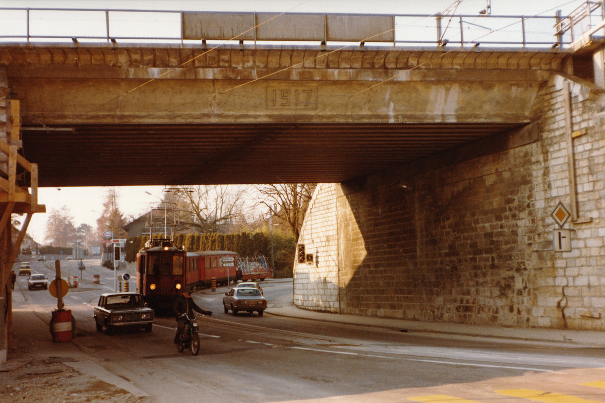 Nyon - Saint-Cergue - Morez NStCM.
Zur heutigen Zeit kaum mehr denkbar. Die damalige NStCM-Streckenführung als Strassenbahn zur Endhaltestelle Nyon. Ein Sportzug auf der Rückfahrt aus dem Jura beim Passieren der 1917 erbauten SBB Unterführung im Januar 1979. Besondere Beachtung gilt dem Skiwagen am Zugsschluss.
Die NStCM nimmt seit Juli 2004 in einem neu erbauten unterirdischen Kopfbahnhof in Nyon ihren Anfang.
Nahe der Haltestelle L'Asse findet das jährliche Paléo Festival statt.
Foto: Walter Ruetsch 