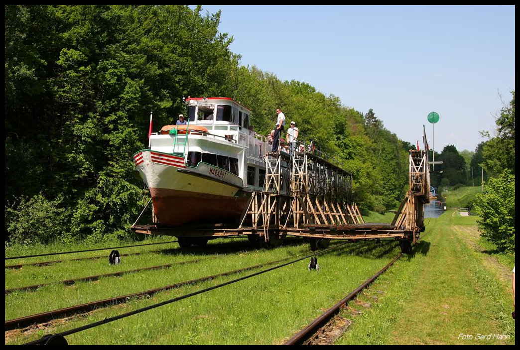 Oberlandkanal bei Buczyniec am 22.05.2012: Der Oberlandkanal in Polen ist heute  eine viel besuchte touristische Attraktion; denn dort wird man als Passagier auf dem Schiff mittels einer Standseilbahn über fünf Berge gezogen. Eine dieser Bergpassagen befindet sich bei Buczyniec. Am 22.05.2012 hielt ich eine solche Fahrt im Bild fest: Während hier der bergwärts gezogene Rollwagen mit der MARABU beladen ist, kommt der Gegenwagen an diesem Tag ohne Last entgegen und fährt talwärts.