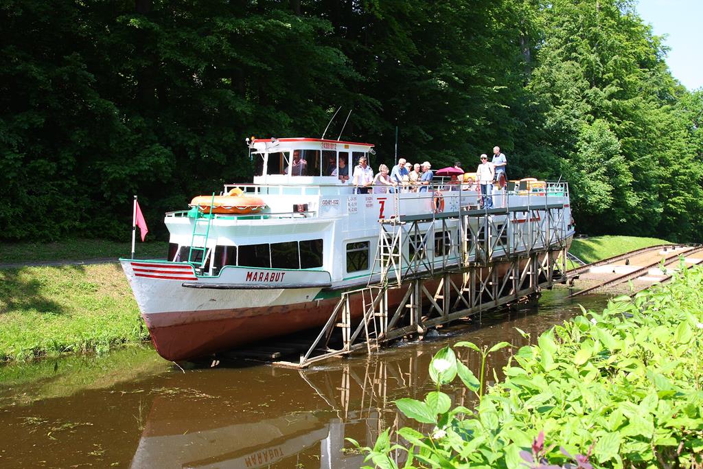 Oberlandkanal bei Buczyniec am 22.05.2012: Der Oberlandkanal in Polen ist heute eine viel besuchte touristische Attraktion; denn dort wird man als Passagier auf dem Schiff mittels einer Standseilbahn über fünf Berge gezogen. Eine dieser Bergpassagen befindet sich bei Buczyniec. Am 22.05.2012 hielt ich eine solche Fahrt im Bild fest: Hier taucht der Rollwagen am oberen Flusslauf wieder ins Wasser ein, so dass die Marabu wieder aufschwimmen kann.