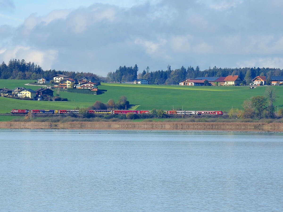 ÖFB-Railjet braust als RJ645 seinem nächsten Halt Neumarkt-Wallersee entgegen, und fügt sich mit seiner bunten Farbgebung in das landschaftliche Bild des genannten Sees im Salzburger Alpenvorland; 221106